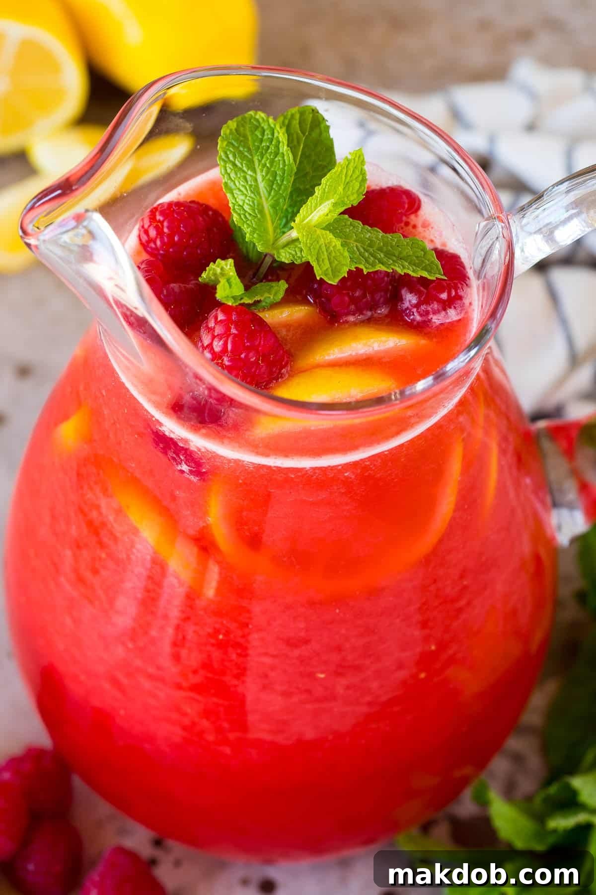 A large glass pitcher filled with homemade raspberry lemonade, garnished generously with fresh lemon slices and mint sprigs, showcasing a beautiful, ready-to-serve beverage.