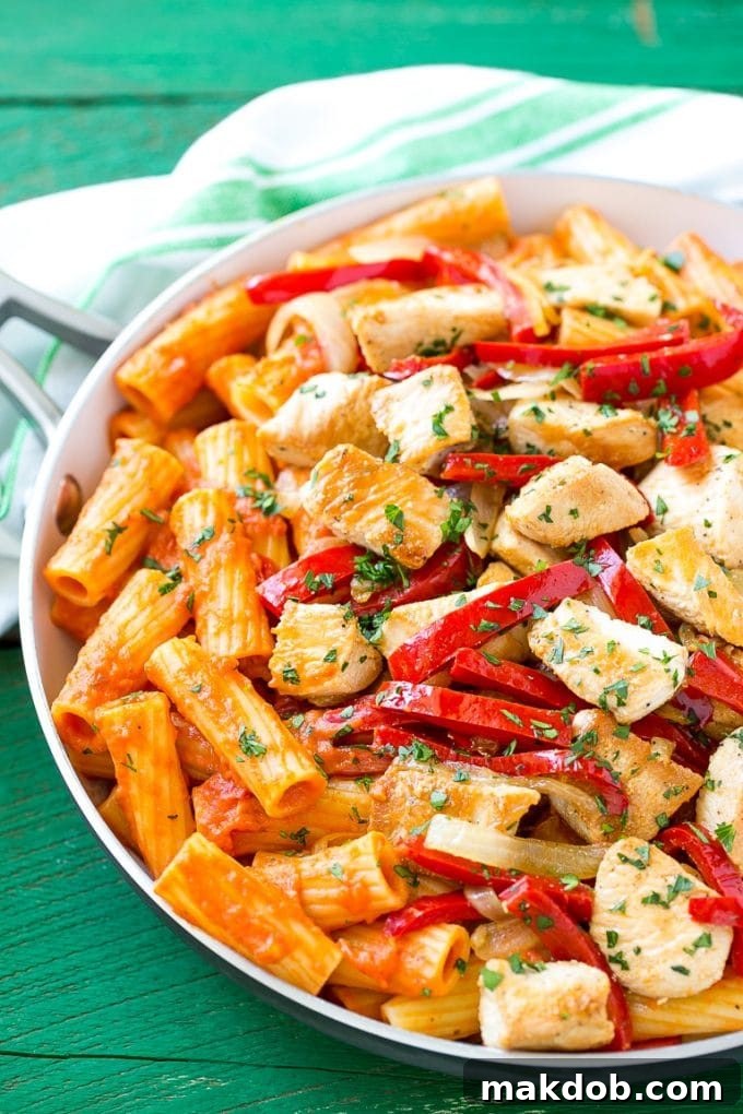 A pan full of rich chicken riggies pasta topped with thinly sliced red bell peppers and fresh parsley.