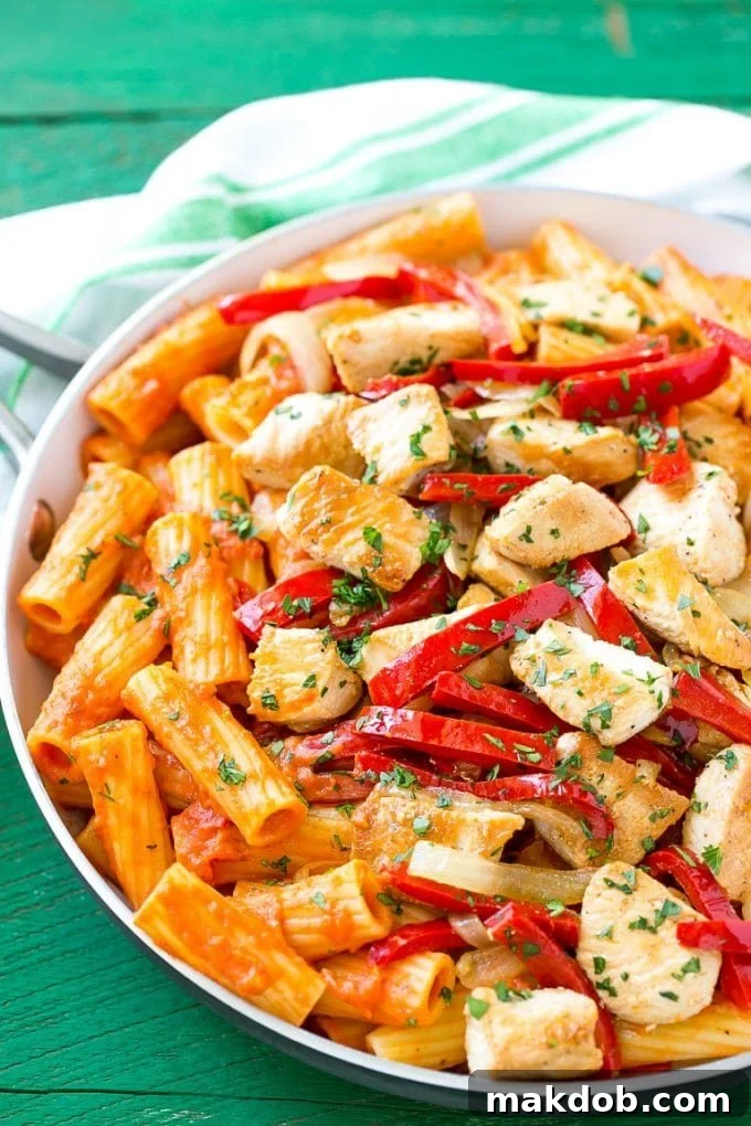 A skillet full of delectable chicken riggies, topped with vibrant bell peppers, thinly sliced onion, and fresh chopped parsley, ready for serving.