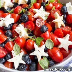 A vibrant Red, White & Blue Caprese Salad, featuring fresh blueberries, cherry tomatoes, and mozzarella pearls.