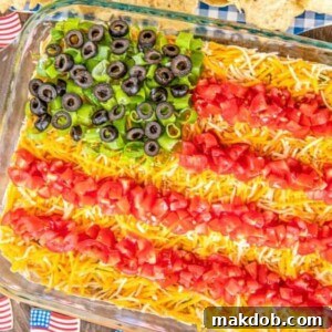 An impressive 7 Layer Taco Dip, artfully decorated with tomatoes, cheese, and olives to resemble an American flag.