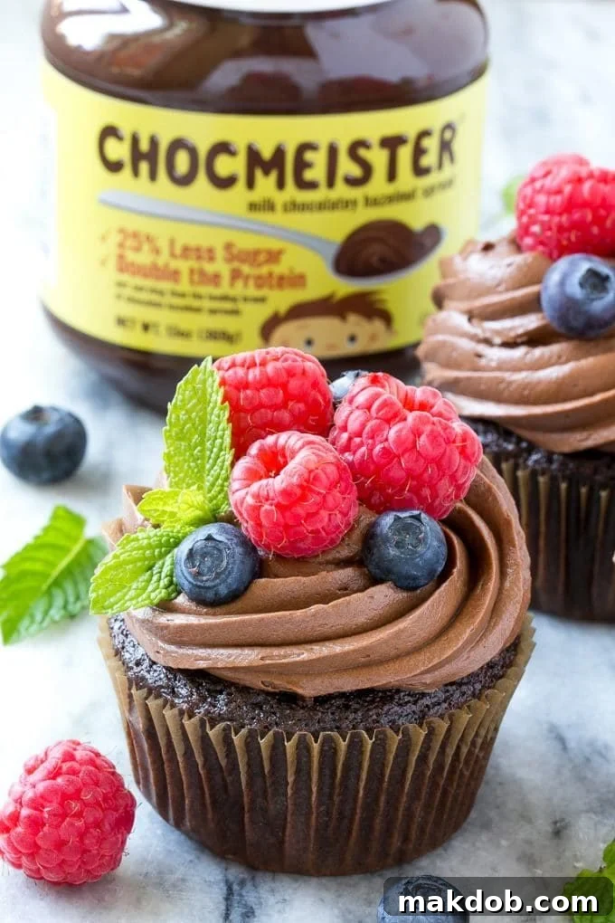Three Nutella cupcakes arranged artfully with vibrant raspberries and blueberries, showcasing the creamy frosting and inviting presentation.