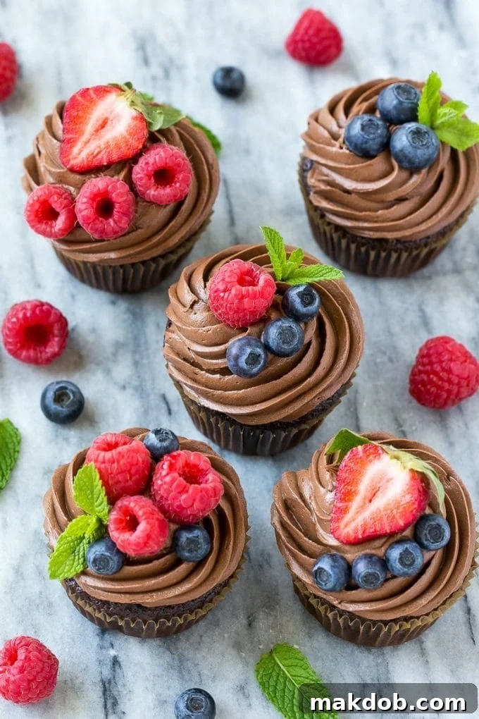 Beautifully decorated chocolate hazelnut cupcakes topped with a rich swirl of frosting, fresh berries, and a sprig of mint. Perfect for a festive table.