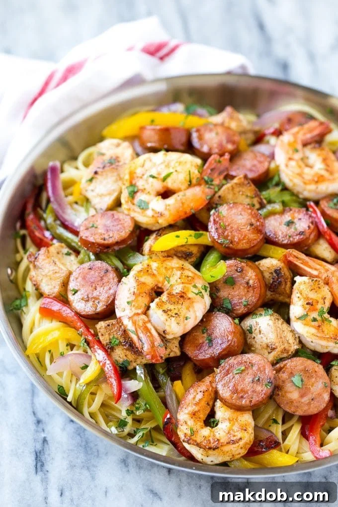 A pan of creamy Cajun jambalaya pasta brimming with shrimp, chicken, andouille sausage, and a colorful mix of bell peppers and onions.