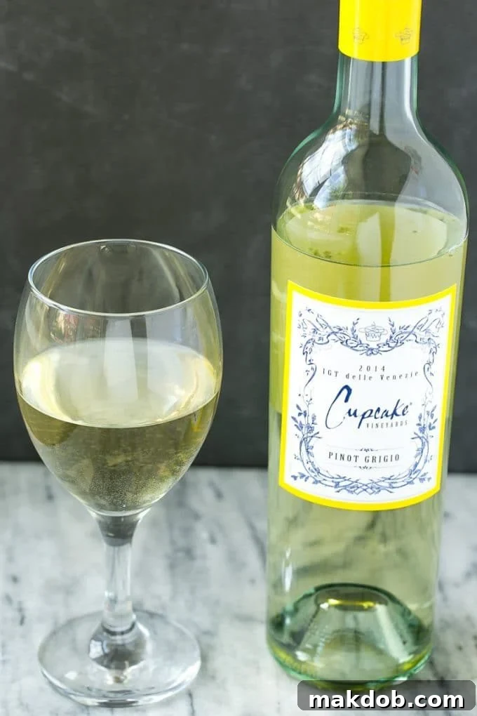 A bottle of elegant Cupcake Pinot Grigio wine next to a full glass, perfect for pairing with a gourmet meal.