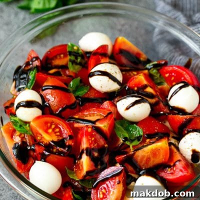 Caprese salad with tomatoes, fresh mozzarella balls, and green basil leaves, lightly dressed with balsamic glaze, captured in a square format.