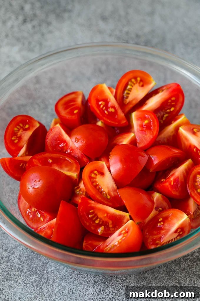 A bowl filled with freshly quartered ripe red tomatoes, showcasing their vibrant color and juicy texture, meticulously prepared and ready for assembly into a Caprese salad.