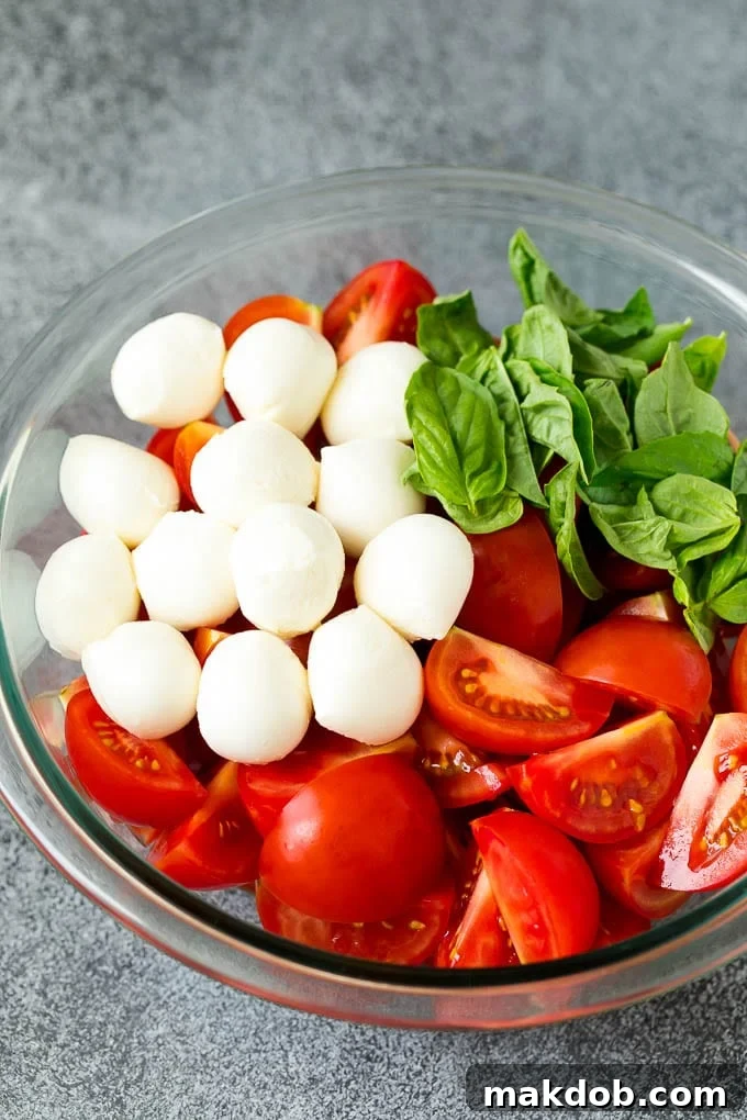 A vibrant bowl of Caprese salad with fresh red tomatoes, creamy white mozzarella pearls, and bright green basil leaves, lightly tossed together and beautifully arranged, ready for the final balsamic drizzle.