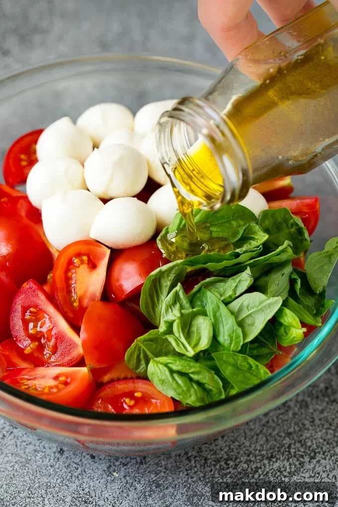 A stream of golden extra virgin olive oil being gracefully poured over a vibrant mixture of red tomatoes, white fresh mozzarella balls, and bright green basil leaves in a bowl, enhancing the colors and flavors with a luxurious sheen.