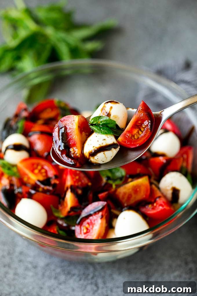 A serving spoon lifting a generous portion of Caprese salad, showcasing juicy tomato pieces, soft fresh mozzarella balls, and aromatic basil leaves, perfectly dressed and ready to enjoy, highlighting its irresistible appeal.