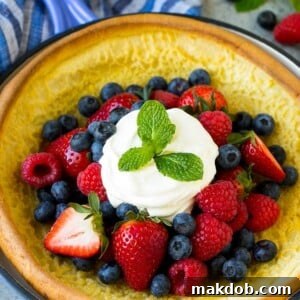 A Dutch baby puffed pancake in a skillet, topped with berries and whipped cream.