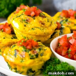 Breakfast egg muffins on a serving plate garnished with tomato and herbs.