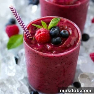 A glass of frozen fruit smoothie in crushed ice, garnished with berries and mint.
