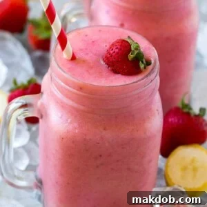 A mason jar mug of strawberry banana smoothie with fresh strawberry on top.