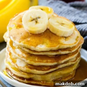 A stack of banana pancakes with banana slices and maple syrup.