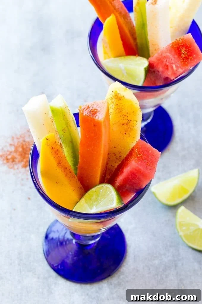 Mexican fruit cups with an assortment of fruit, topped with chili lime seasoning and lime wedges.