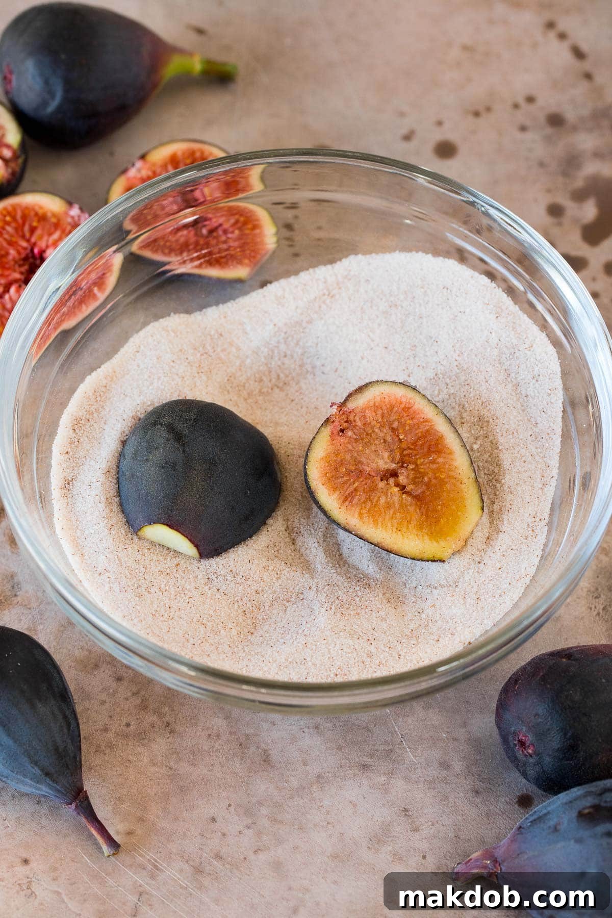 Luscious Roasted Figs 5 Fresh fig halves meticulously dipped in a bowl of aromatic cinnamon sugar mixture, preparing for roasting.