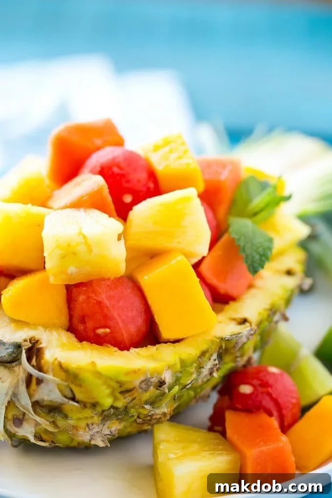 A pineapple half filled with colorful melon, papaya, and mango chunks, ready to be seasoned.