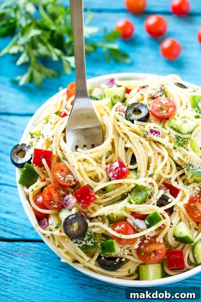 A vibrant bowl of spaghetti salad, brimming with colorful vegetables and cheese, with a serving fork ready to scoop.