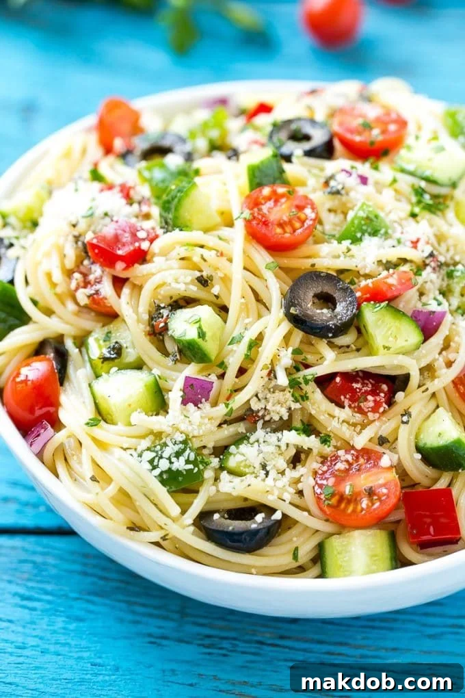 A large bowl of cold pasta salad featuring vibrant cucumbers, black olives, and a generous sprinkle of parmesan cheese.