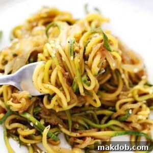 Stir-fry zucchini noodles and onions on a fork, ready to be enjoyed.