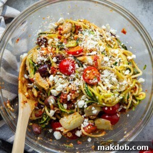 A vibrant bowl of Mediterranean zucchini noodle salad, rich with fresh ingredients.