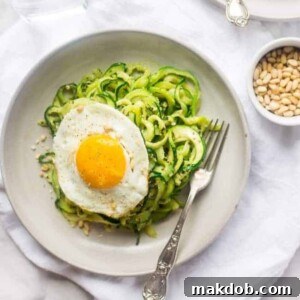 A plate of zucchini noodles with pesto, topped with perfectly fried eggs.