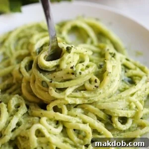 A fork twirling luscious zucchini noodles coated in creamy avocado pesto.
