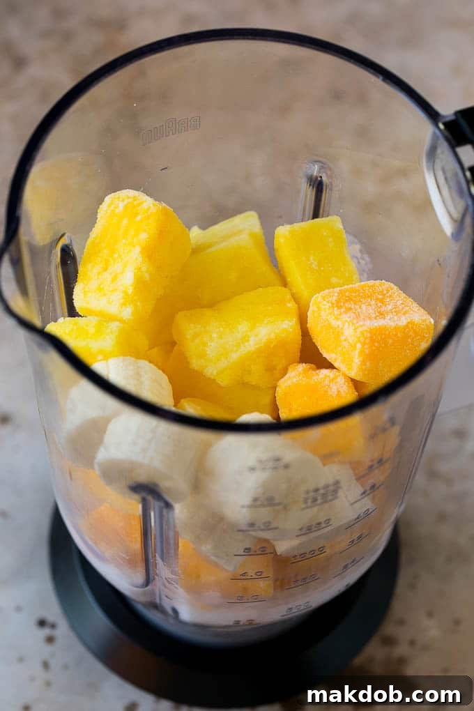 How to Make Tropical Smoothie | Blender Ready Ingredients Pineapple, mango, banana, and coconut milk in a blender, ready to be blended into a delicious tropical smoothie.