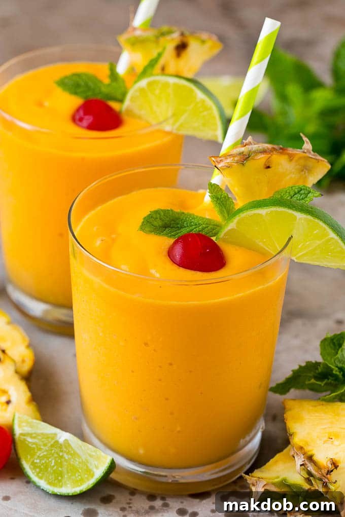 Island Escape Smoothie 2 Two vibrant mango pineapple smoothies, garnished with fresh maraschino cherries and mint sprigs, ready to enjoy.