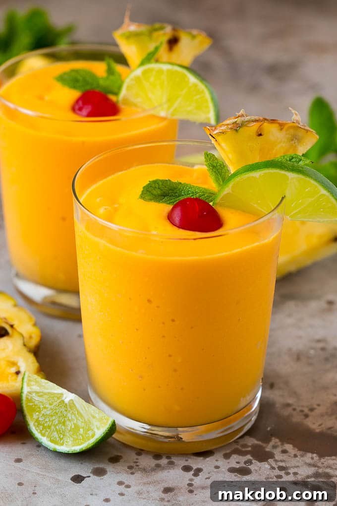 Customize Your Tropical Smoothie | Flavorful Combinations Two vibrant tropical smoothies expertly garnished with fresh mint, zesty lime wedges, and elegant pineapple slices, ready to be served.
