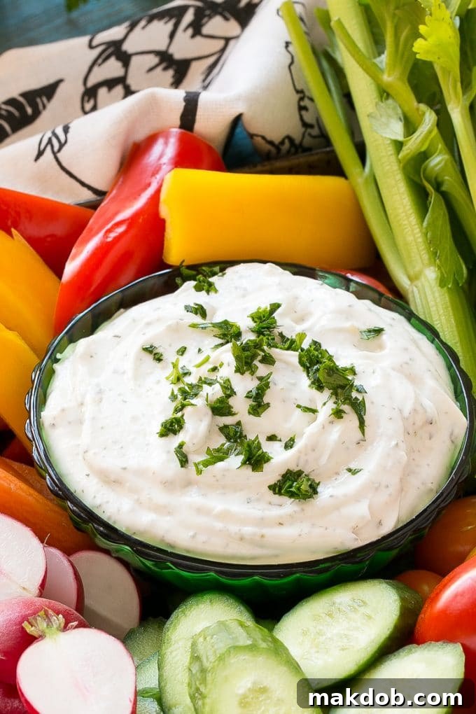 Homemade Ranch Dip Recipe | Homemade Ranch Powder | Homemade Ranch Dressing | Best Ranch Dip #ranch #dip #appetizer #snack #dinneratthezoo A close-up shot of homemade ranch dip in a white bowl, generously garnished with finely chopped fresh parsley. The dip is surrounded by a colorful assortment of fresh vegetables, including bright red bell peppers, crisp green cucumber slices, and crunchy carrot sticks, highlighting its freshness and appeal.