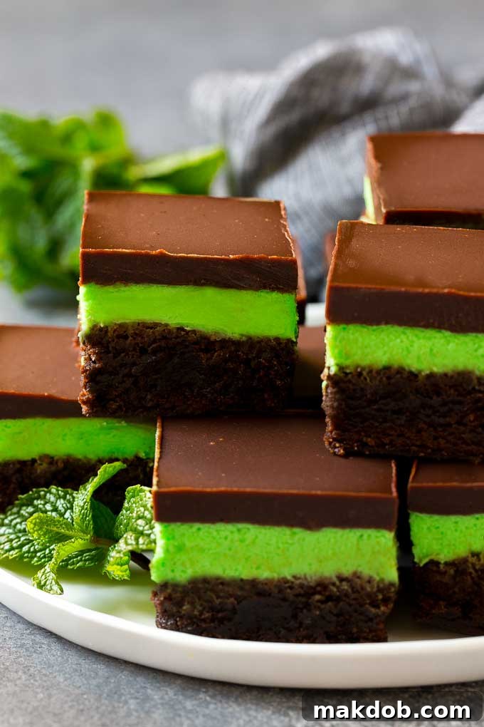 Mint Brownies Recipe | Layered Brownies | Frosted Brownies #brownies #chocolate #frosting #mint #dessert #dinneratthezoo Layered mint brownies with frosting on a serving plate, garnished with fresh mint.