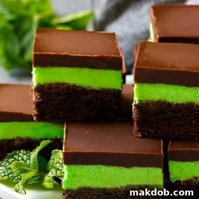 Layered mint brownies with frosting on a serving plate, garnished with fresh mint.