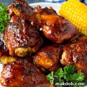 A large platter of perfectly grilled BBQ chicken, garnished with fresh corn on the cob and bright parsley.
