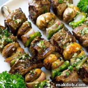 Delicious steak kabobs featuring mushrooms, vibrant red onion, and colorful bell peppers, all brushed with savory garlic butter.