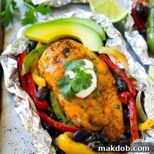 Cooked chicken breasts covered in melted cheese, surrounded by vibrant peppers, onions, and black beans, all perfectly enclosed within a foil packet.