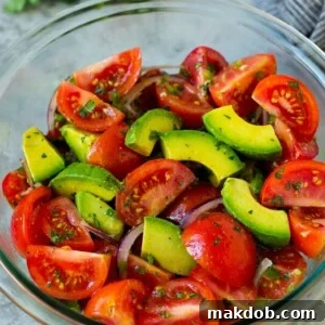 A refreshing tomato avocado salad with thinly sliced red onion and a bright cilantro lime dressing.