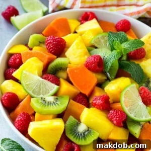 A vibrant bowl of tropical fruit salad, brimming with fresh mango, raspberries, papaya, kiwi, and pineapple, all tossed in a zesty honey lime dressing.