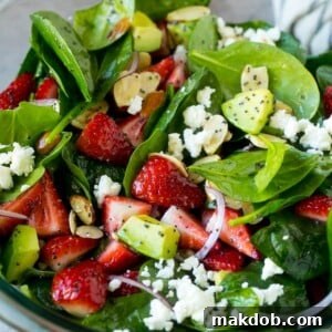 A vibrant bowl of strawberry spinach salad, featuring poppy seed dressing, crumbled feta cheese, and perfectly sliced avocado.