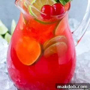 A glass pitcher of vibrant cherry limeade, elegantly garnished with fresh lime slices and bright maraschino cherries.