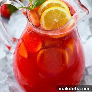 A pitcher of refreshing strawberry lemonade, garnished with vibrant lemon slices and fresh mint leaves.