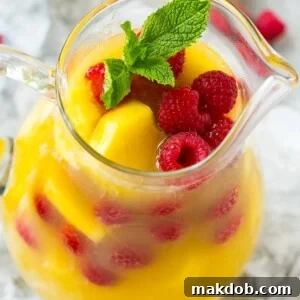 A pitcher of delightful pineapple punch, featuring fresh pineapple chunks, juicy raspberries, and fragrant mint leaves.
