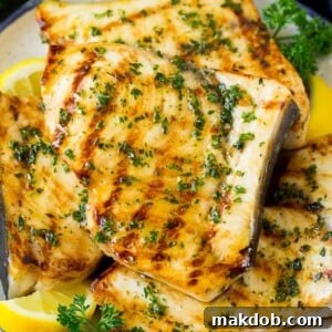 A plate of perfectly grilled swordfish steaks, lightly charred and topped with fresh herbs.