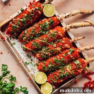 A vibrant tray laden with several Flaming Hot Cheetos Elotes, each grilled corn on the cob lavishly coated in a fiery red Cheetos dust. Drizzled with creamy lime mayo and chipotle aioli, and sprinkled with fresh green cilantro, these elotes promise a bold, spicy, and irresistible flavor experience that's both playful and intensely satisfying.