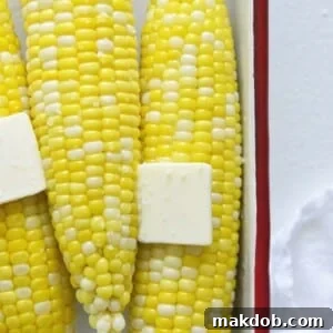 A close-up image of perfectly microwaved corn on the cob, glistening with a generous pat of melted butter on top, ready to eat.
