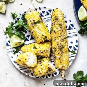 A close-up image of grilled cilantro lime corn on the cob, featuring vibrant green cilantro and bright lime wedges. The corn shows subtle char marks, indicating a perfect grill, and is seasoned with red pepper flakes, promising a refreshing yet spicy kick.