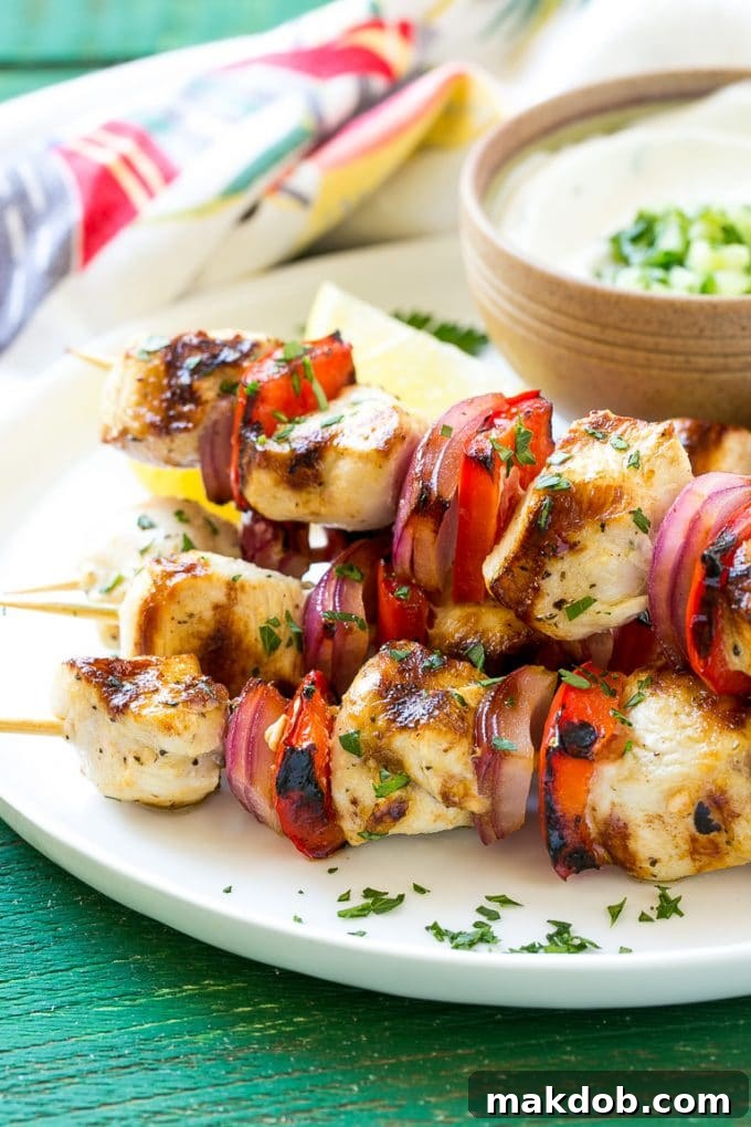 Greek Chicken Kabobs | Grilled Chicken Kabobs | Healthy Chicken Recipe | Greek Chicken #greekfood #chicken #grilling #grilledchicken #kabobs #dinner #dinneratthezoo A stack of three beautifully grilled Greek chicken skewers, interspersed with bright red bell peppers and red onions, garnished with fresh parsley.