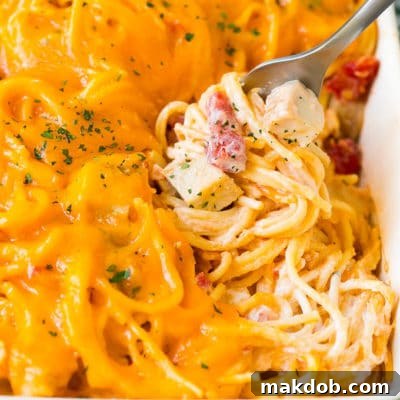 A fork serving up a portion of creamy chicken spaghetti, showcasing the golden melted cheese and tender chicken.
