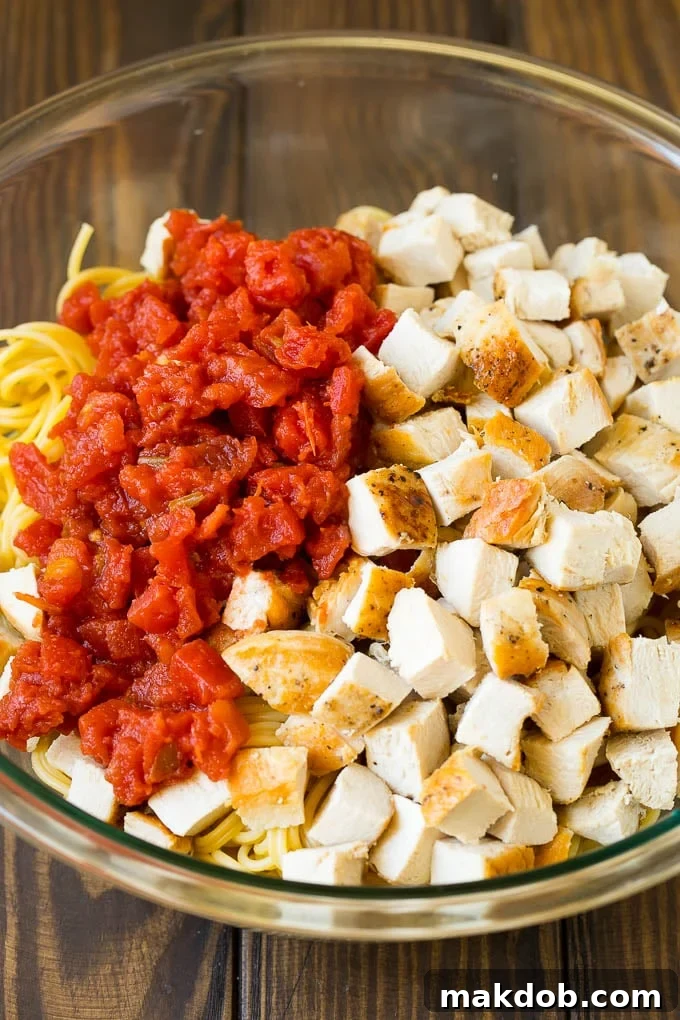 Diced chicken, zesty tomatoes, and spaghetti coated in a creamy cheese sauce, ready for baking.